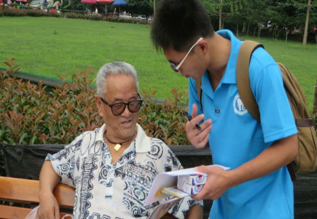 实践队员陈建給在广场休息的老人做问卷调查。